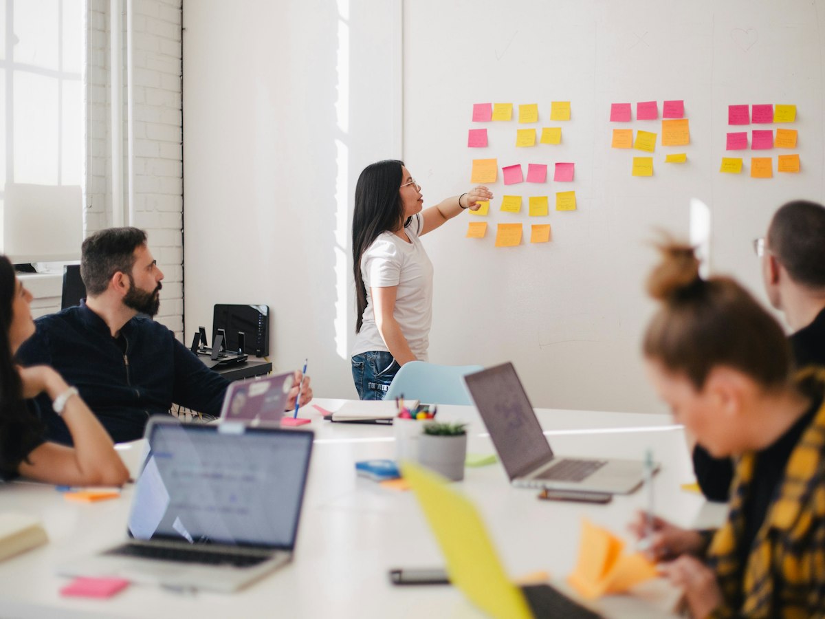 A woman pointing at pink and yellow sticky notes while colleagues sit around laptops