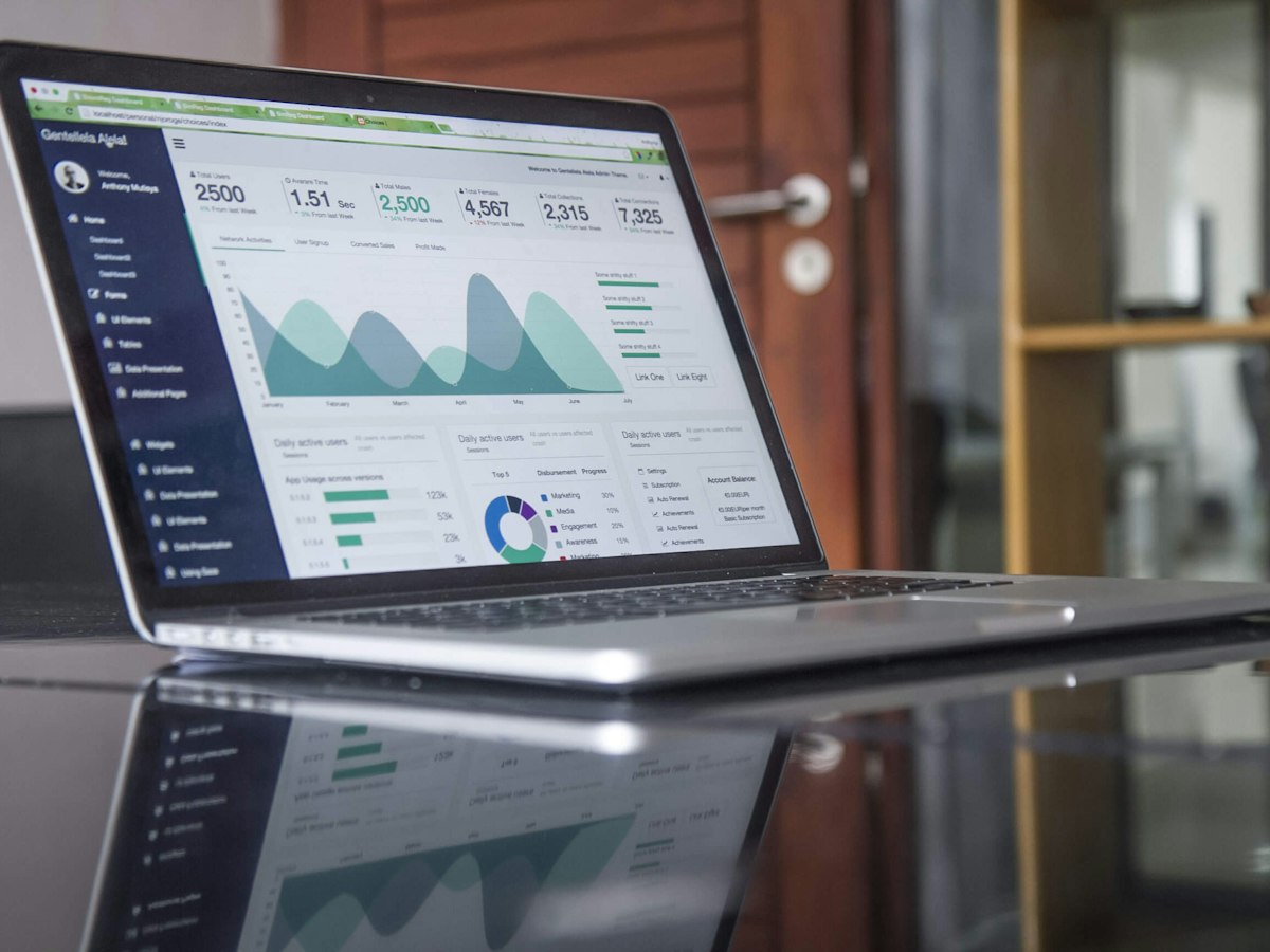 A laptop on a glass desk showing a dashboard of charts and numbers