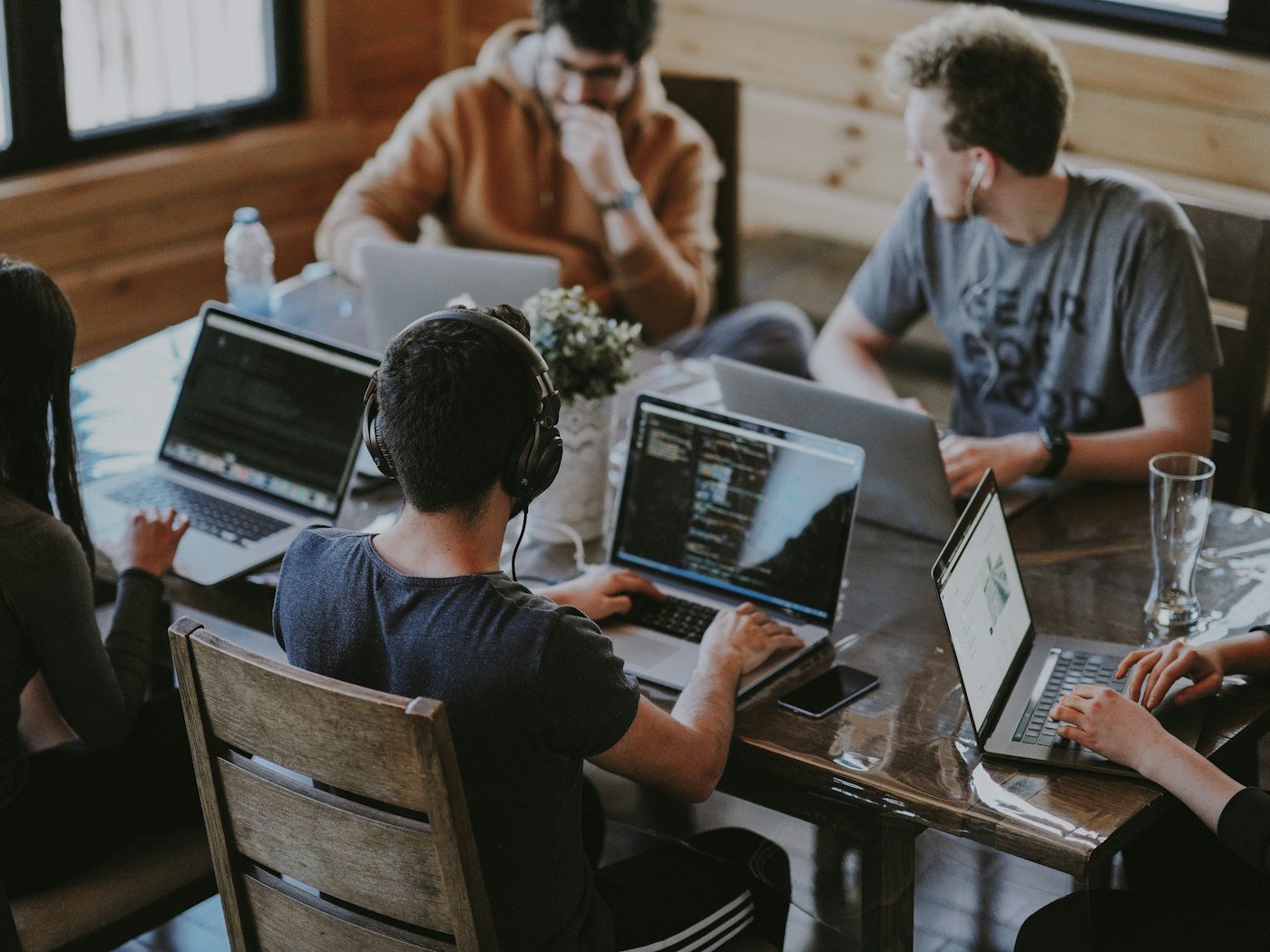 Developers around a wooden table, each working on a laptop with code on the screens